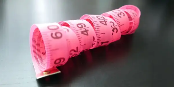 Różowa miarka krawiecka zwinięta w spirale, z widocznymi centymetrami. Idealna do określenia rozmiaru buta 2 latka.