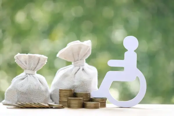 Symbol osoby na wózku inwalidzkim obok worków z pieniędzmi i monet sugeruje świadczenie wspierające kwoty.