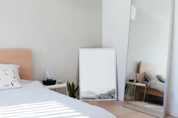 Jasne, minimalistyczne lustro w sypialni feng shui odbija łóżko i tworzy wrażenie większej przestrzeni.