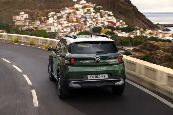 Zielony Citroën C3 Aircross z białym dachem jedzie krętą drogą w górach, z widokiem na kolorowe miasteczko i morze.