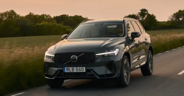 Ciemnoszary Volvo XC60 2025 jedzie drogą wśród zieleni o zachodzie słońca.