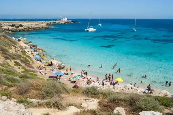 Spiaggia di Favignana, dove si trova questo paradiso azzurro con gente che si gode il sole e il mare cristallino, con barche all'orizzonte.