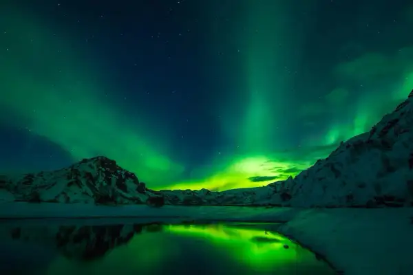 Reykjavik zorza polarna kiedy? Zielone światła tańczą nad ośnieżonymi górami i spokojną wodą.