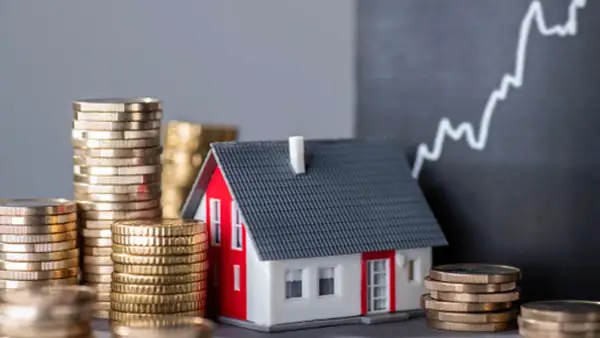 Casa modelo rodeada de pilas de monedas, con un gráfico ascendente al fondo, sugiriendo un estudio de solvencia y el valor de la inversión inmobiliaria.