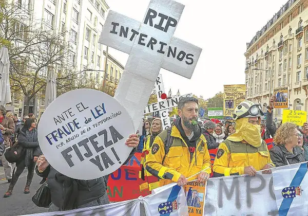 Manifestantes protestan contra el fraude de ley y el abuso de temporalidad, exigiendo fijeza. Un cartel en forma de cruz dice "RIP INTERINOS", reflejando el deseo de no ser interino toda la vida.