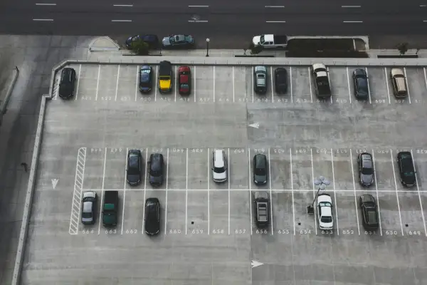 Widok z góry na parking. Samochód cofający na parkingu, kto ma pierwszeństwo? Wiele zaparkowanych aut.