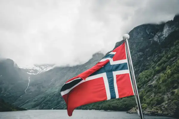 Norweska flaga na tle fiordu i gór. Marzysz o pracy w Norwegii? Sprawdź najlepiej płatne zawody w Norwegii!