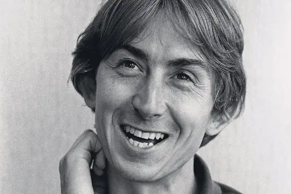 Black and white close-up portrait of Mark Hollis of Talk Talk smiling with his hand near his face.