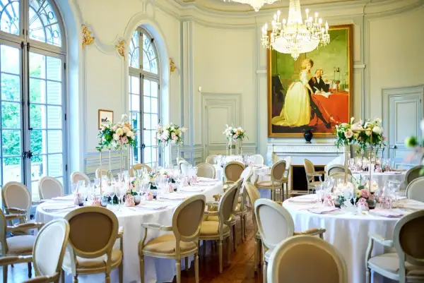 Salle de réception élégante avec tables rondes dressées pour un mariage. Un tableau ancien domine la pièce, offrant une idée de plan de table mariage.
