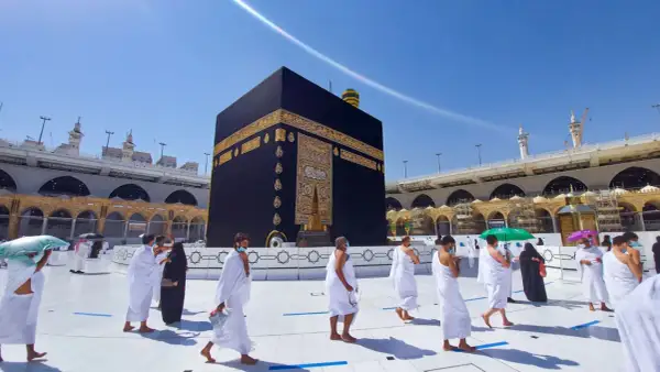Pielgrzymi w białych strojach okrążają Kaabę, święte miasto islamu, w słoneczny dzień.