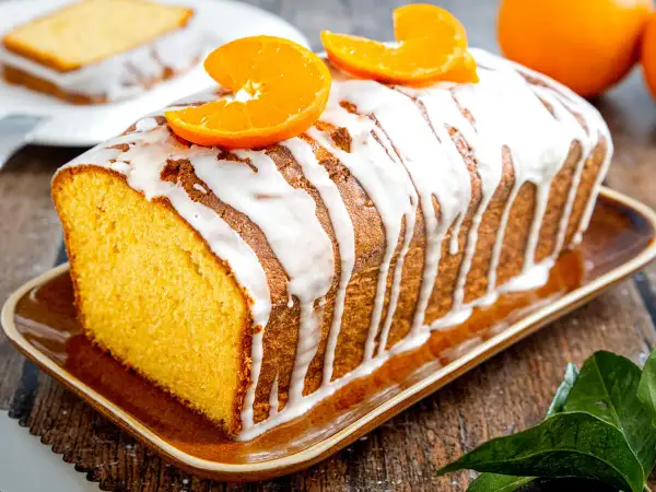 Omas saftiger Orangenkuchen, mit Zuckerguss und frischen Orangenscheiben garniert, duftet herrlich auf dem rustikalen Holztisch.