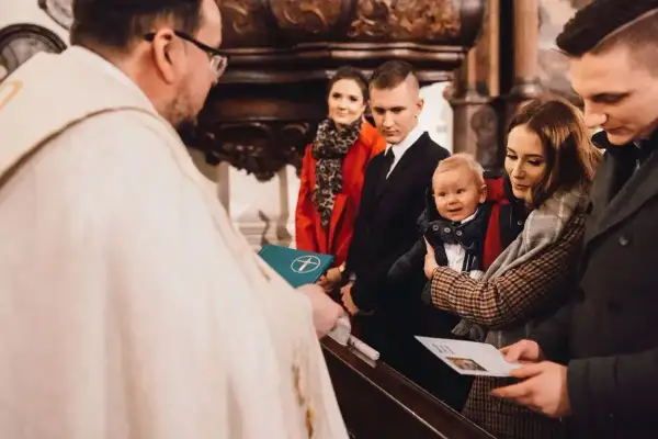 Rodzina świętuje, kiedy chrzci się dzieci. Ksiądz błogosławi niemowlę trzymane przez matkę, podczas gdy ojciec i chrzestni patrzą z dumą.