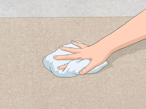 Mano che tampona una macchia su tessuto beige con un panno bianco. Guida su come togliere macchia d'olio.