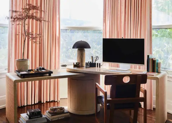 Stylish personal office decor ideas: a modern desk with a computer, lamp, and plant, framed by soft pink curtains.