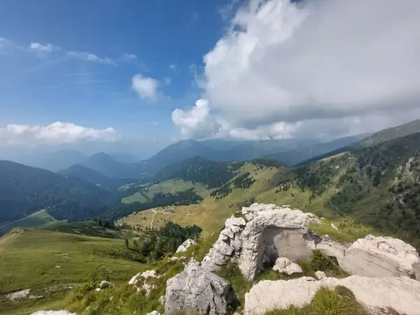 Rovine di un bunker sul **Castello Tesino**, con vista su verdi valli e montagne nebbiose sotto un cielo azzurro e nuvoloso.