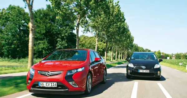 Czerwona Opel Ampera i czarny samochód jadą drogą otoczoną drzewami.