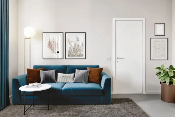 Divano blu intenso con cuscini tortora e grigi. Un tavolino bianco e un tappeto scuro completano l'ambiente.