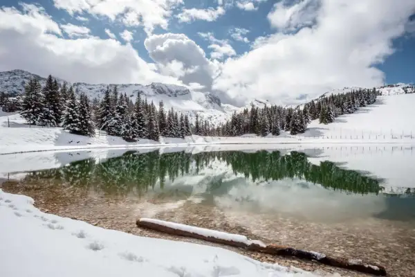 Lac d'altitude enneigé, reflétant les sapins et les montagnes. Idéal pour découvrir que faire autour de Villard de Lans en hiver.