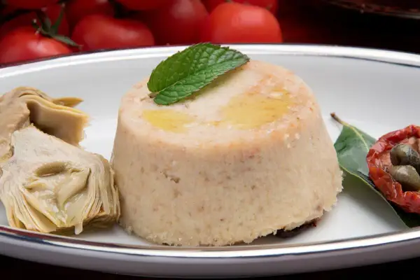 Delizioso flan di carciofi, guarnito con menta e accompagnato da carciofi sott'olio, pomodori secchi e capperi.
