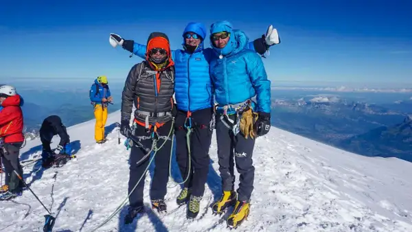 Drei Bergsteiger auf dem Gipfel des Monte Blanc, umgeben von Schnee und einer atemberaubenden Aussicht.