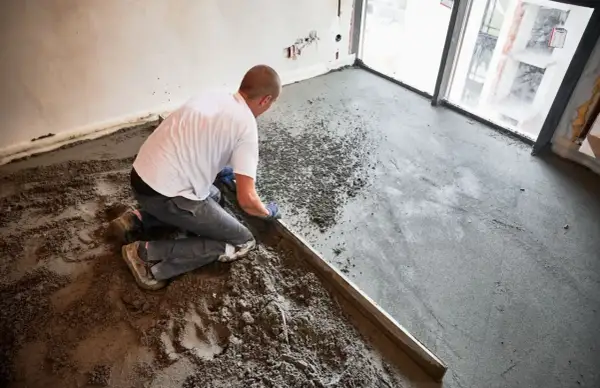 Budowlaniec klęczy, wyrównując świeży jastrych za pomocą łaty.
