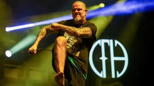 Phil Anselmo z Pantery w Polsce, z mikrofonem w dłoni, na tle sceny z oświetleniem.