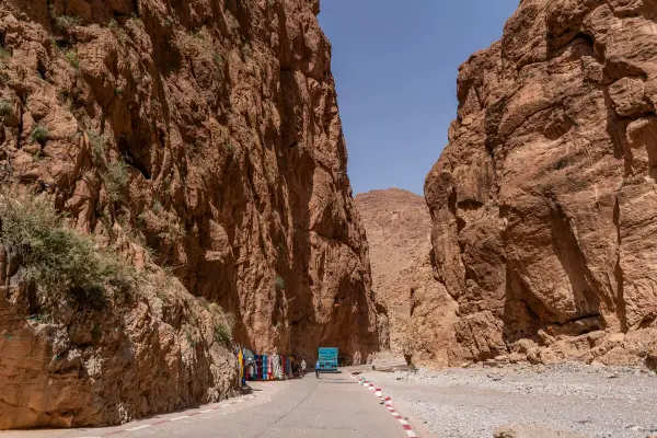 Die Todra-Schlucht mit ihren steilen, roten Felswänden. Eine Straße führt hindurch, gesäumt von Souvenirständen und einem blauen LKW.