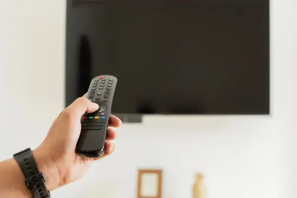 Dłoń trzymająca pilot do telewizora, zastanawiająca się, czy telewizor pobiera dużo prądu.