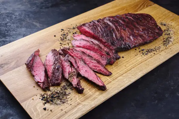 Perfekt zubereitetes Skirt Steak, in Scheiben geschnitten, liegt auf einem Holzbrett. Gewürze und Pfeffer sind verstreut.