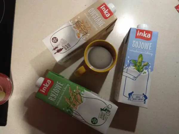 Trzy kartony napojów Inka (owsiane, sojowe, ryżowe) i kubek kawy.