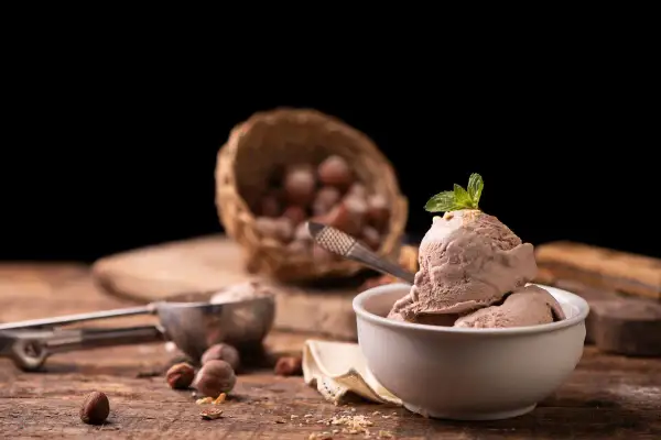 Delizioso gelato alla nocciola appena fatto con la gelatiera, guarnito con menta fresca. Nocciole in un cesto sullo sfondo.