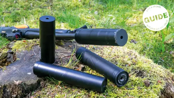 Tre ljuddämpare för jakt, en 125 mm, ligger på en mossig stubbe bredvid ett gevär. En guide hjälper dig att välja rätt.