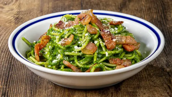 Un piatto invitante di pasta con spinaci e croccante pancetta, cosparso di formaggio grattugiato.
