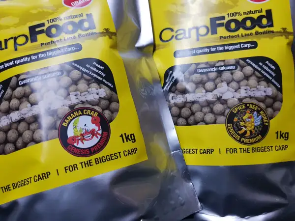 Dwie paczki z żółtymi etykietami zawierają kulki na karpia. Na opakowaniach widnieje napis "CarpFood" i grafika z pszczołą.