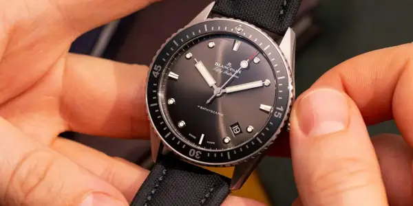 Manos ajustando un reloj automático Blancpain Fifty Fathoms Bathyscaphe con correa de tela negra.