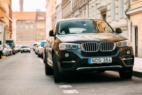 Czarny SUV zaparkowany na ulicy, przypominający o przepisach dotyczących zastawiania bramy wjazdowej.