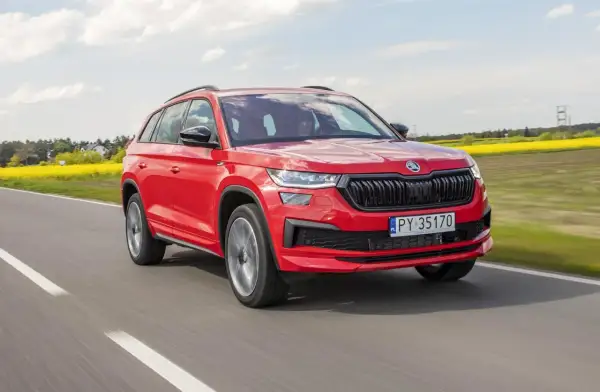 Czerwony Skoda Kodiaq 2023 pędzi po drodze, mijając kwitnące pola rzepaku.