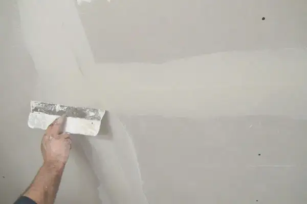Hand verspachtelt Rigipsplatten mit einem Spachtel. Die Naht wird geglättet, um eine ebene Oberfläche für die weitere Bearbeitung zu schaffen.