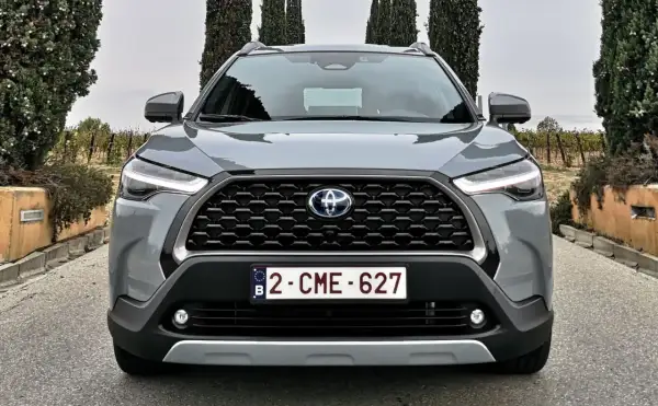 Szary SUV Toyota Hybryda 2022 z przodu, z grillem i światłami LED, na tle winnicy i drzew.