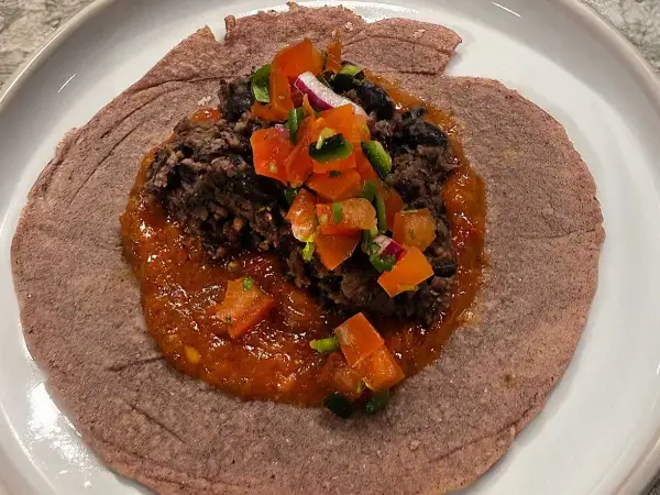 En lila tortilla med en klick refried beans, toppad med salsa och hackad lök.