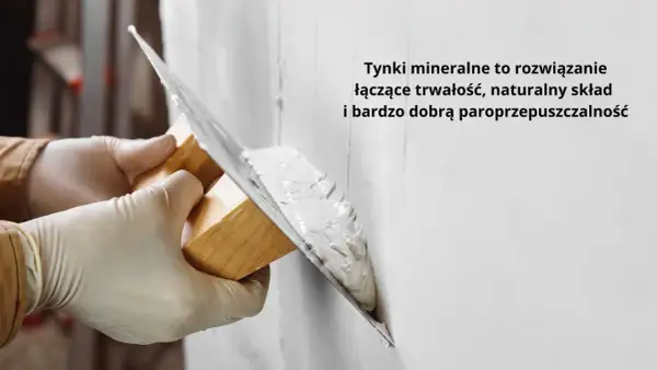 Ręce w rękawiczkach nakładają tynk na ścianę kielnią. To obrzutka, która zapewnia trwałość i paroprzepuszczalność.