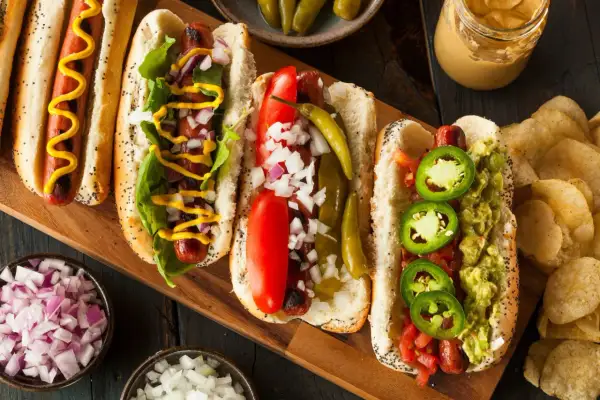 Cztery pyszne hot dogi z różnymi dodatkami: musztarda, cebula, pomidor, papryczki i guacamole.