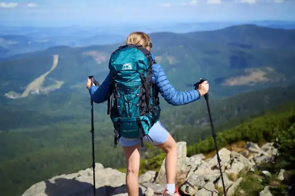 Kobieta z turkusowym plecakiem w góry, z kijkami trekkingowymi, podziwia panoramę. Idealny plecak na górskie wędrówki.