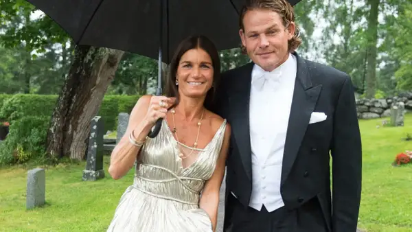 Sian Persson och hennes man, klädda för fest, delar ett paraply i regnet.