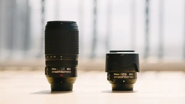 A long telephoto lens stands next to a compact wide-angle lens, showcasing the difference between wide angle vs telephoto perspectives.
