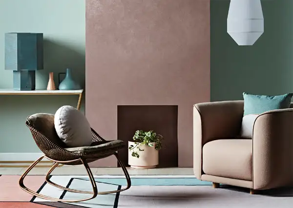 Simulazione abbinamento colori pareti: un salotto con poltrona in vimini, camino rosa e divano beige, su un tappeto geometrico.