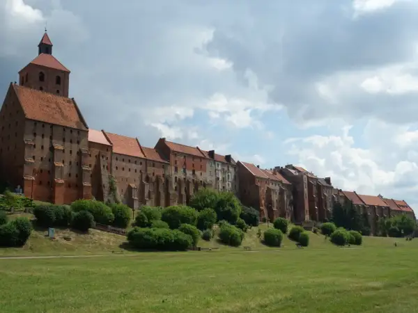 Grudziądz atrakcje: imponująca ceglana twierdza z wieżą i dachem z dachówki, otoczona zielenią i trawnikiem.