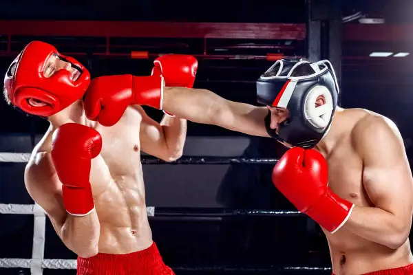 Two boxers in red gloves and headgear clash in a boxing range. One boxer lands a punch, the other reels back.
