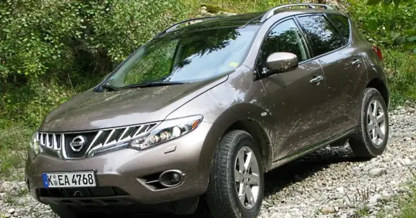Brązowy Nissan Murano na kamienistej drodze, otoczony zielenią.