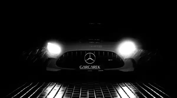 Czarny Mercedes-AMG GT Black Series z włączonymi światłami, stojący na mokrej, metalowej kratce.
